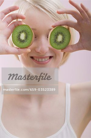 Young woman with two kiwi fruit halves in front of her face