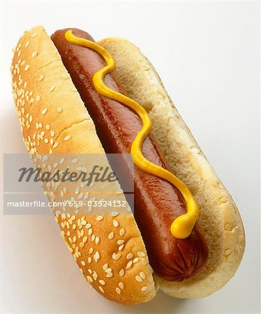 A hot dog with mustard in sesame bun