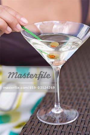 Woman holding green olive on cocktail stick in Martini glass