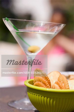 Martini with green olive, crackers, woman in background Martini with green olive, crackers, woman in background