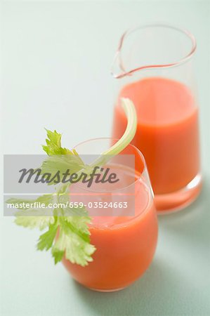 Glass of carrot juice with celery, jug in background