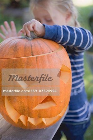 Small girl putting lid on pumpkin lantern