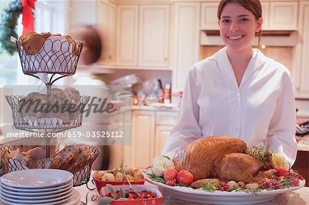 Jeune femme dans la cuisine avec la dinde pour Noël