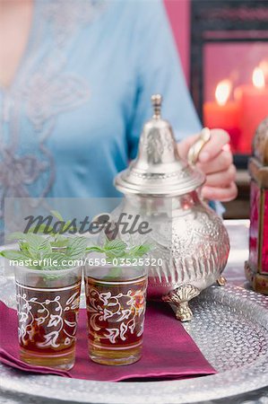 Woman pouring peppermint tea into glasses Woman pouring peppermint tea into glasses