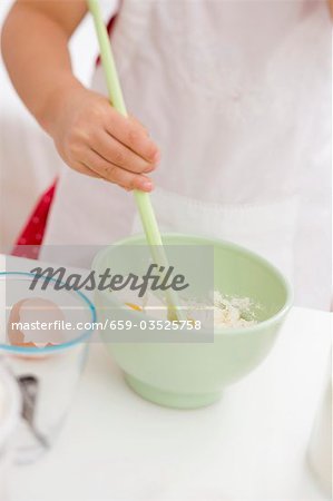 Small girl mixing egg, flour and butter with wooden spoon
