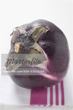 A round aubergine with drops of water on tea towel