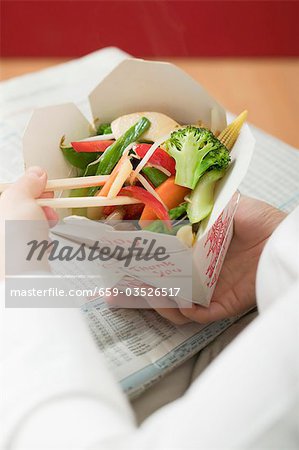 Woman eating Asian vegetable dish out of take-away container