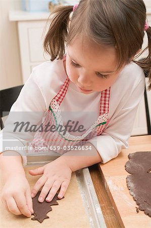 Small girl placing chocolate biscuit on baking tray