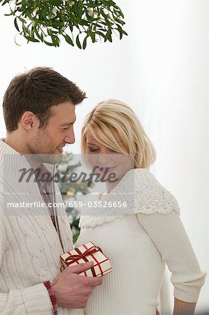 Homme donnant femme cadeaux de Noël sous le gui