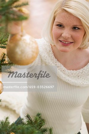 Woman hanging gold bauble on Christmas tree