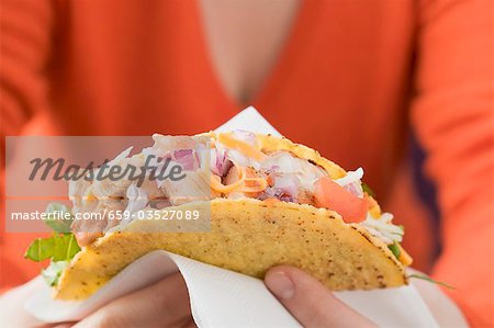 Femme tenant un taco de poulet sur une serviette en papier