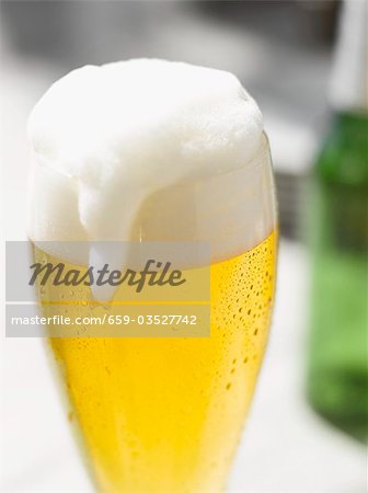 Glass of lager with overflowing head of foam