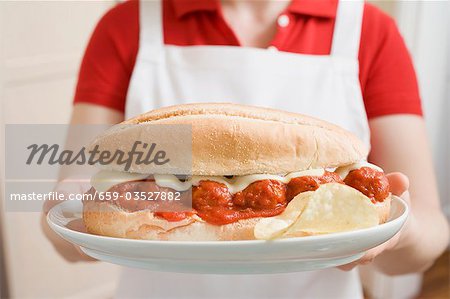 Woman holding giant sandwich filled with meatballs & tomato sauce