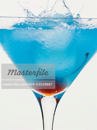 Blue Curaçao cocktail with cocktail cherry and ice cube