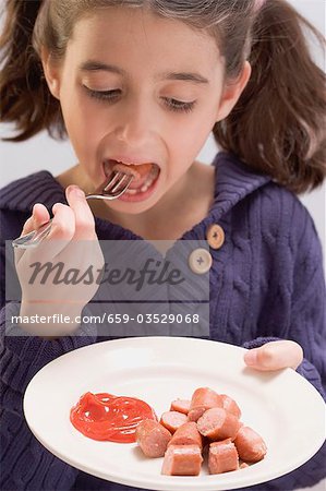 Little girl eating frankfurters with ketchup