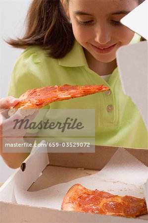 Little girl holding slice of pizza over pizza box