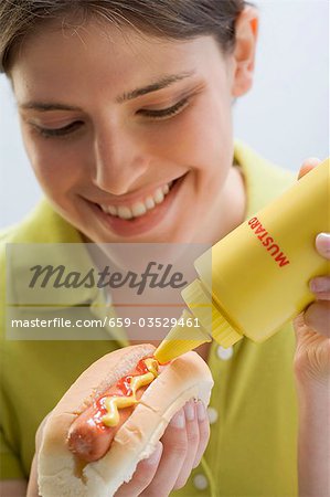 Young woman putting mustard on hot dog