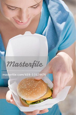 Young woman taking cheeseburger out of polystyrene box