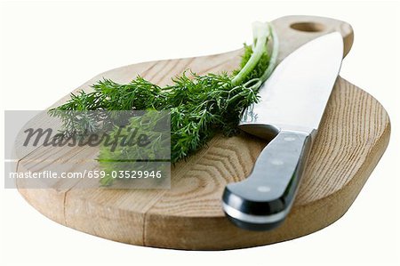 Dill with knife on wooden board