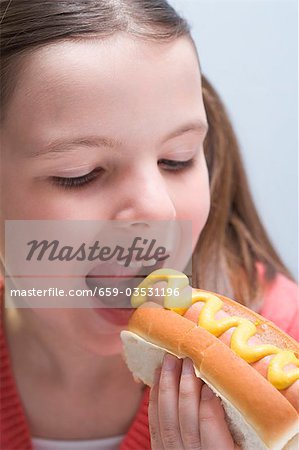 Fille de mordre dans un hot dog à la moutarde