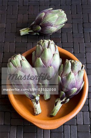 Four baby artichokes with terracotta dish