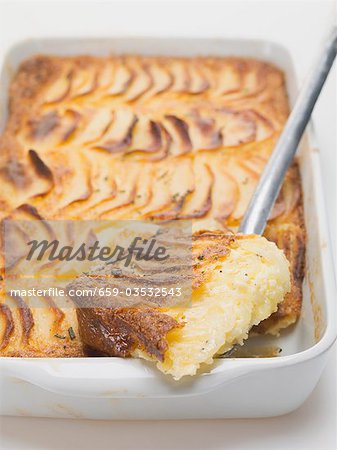 Potato gratin in baking dish with piece on server