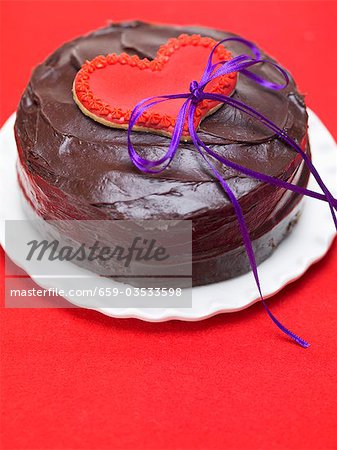 Chocolate cake with red heart-shaped biscuit and bow