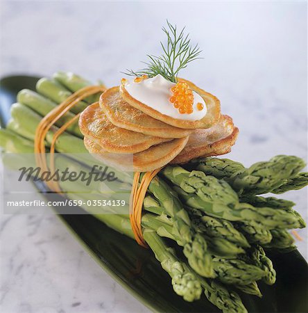 Blinis with sour cream and caviar on green asparagus
