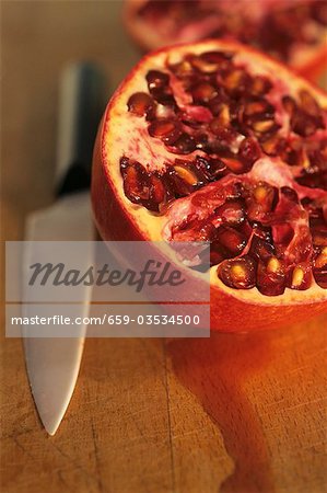 Halved pomegranate on wooden board with knife