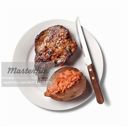 Pork Chop and Baked Sweet Potato on White Plate; White Background