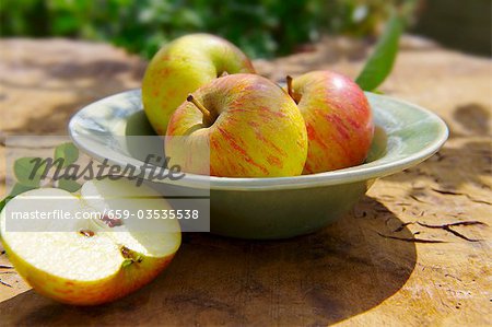 Ganze Äpfel auf einem Teller, einen halben Apfel neben die Platte