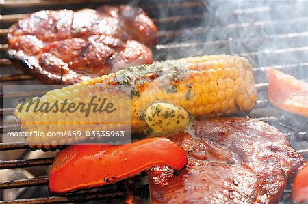 Corn on the cob with herb butter, pork steaks & pepper on barbecue