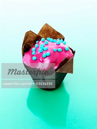 Muffin with pink icing in baking parchment
