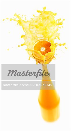 Orange juice splashing out of bottle