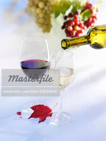 Pouring white wine into glass, glass of red wine, grapes, autumn leaf
