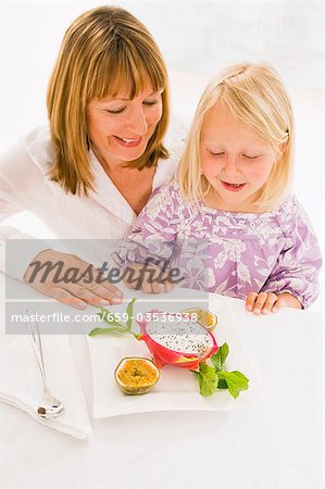 Mutter und Tochter sitzen am Tisch mit Teller mit Obst