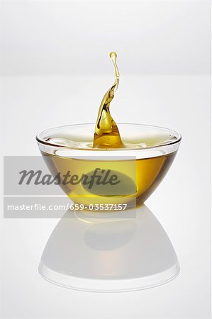 Green olive falling into glass dish of olive oil