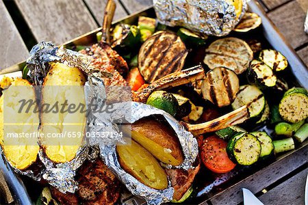 Barbecued vegetables, baked potatoes, lamb chops on barbecue tray