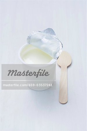 Yoghurt in opened pot, wooden spoon beside it