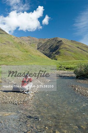 L'homme remplit sa bouteille d'eau lors d'une randonnée le long de la rivière Chandalar dans la chaîne de Brooks au cours de l'été dans l'Arctique de l'Alaska