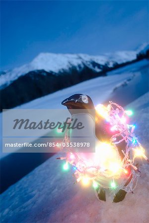 Pingouin en plastique enveloppé dans les lumières d'arbre de Noël assis sur la berge hiver Alaska