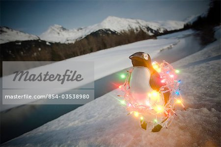 Plastic penguin wrapped in Christmas tree lights sitting on riverbank Winter Alaska