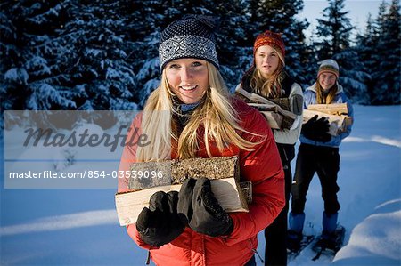 Three young women on snowshoes hauling chopped wood near Homer, Alaska during winter.