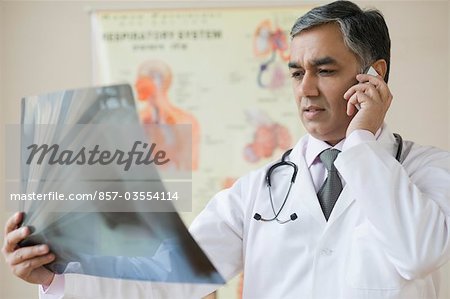 Doctor examining an x-ray and talking on a mobile phone, Gurgaon, Haryana, India