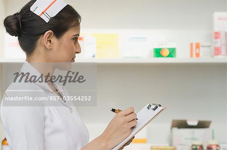 Female nurse writing on a clipboard in a pharmacy, Gurgaon, Haryana, India