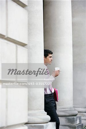 Businessman leaning on pillar outside building holding coffee