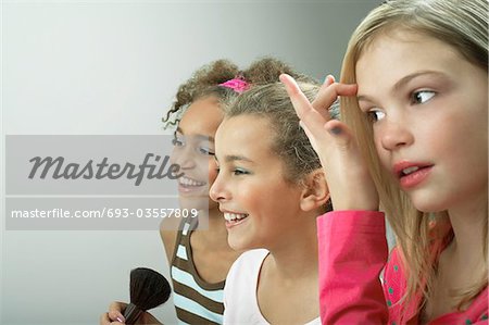 Girls standing side by side putting on make-up, fixing hair