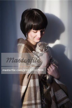 Woman in blanket stands holding kitten