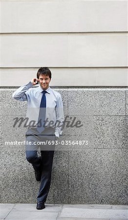 Homme d'affaires sur le téléphone cellulaire se penchant sur le mur du bâtiment