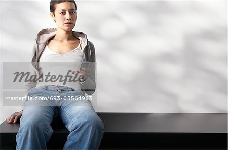 Jeune femme assise à l'intérieur sur le banc se terminant message texte, portrait